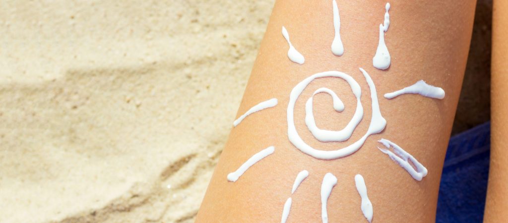 Woman sunbathing on the beach with a drawing of sun on her leg with sunscreen cream